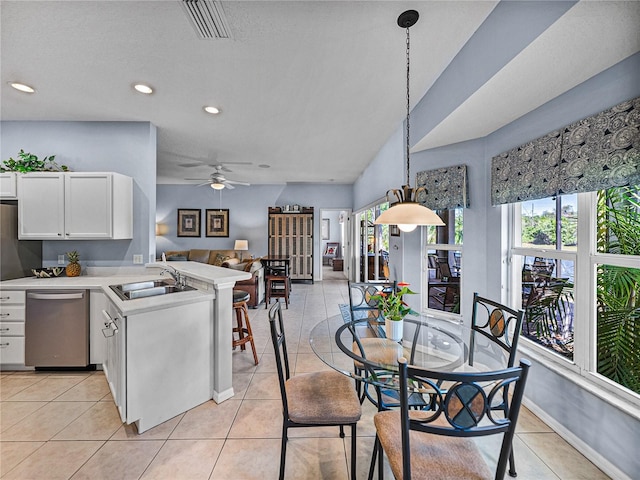 kitchen featuring light countertops, light tile patterned floors, stainless steel dishwasher, a sink, and a peninsula