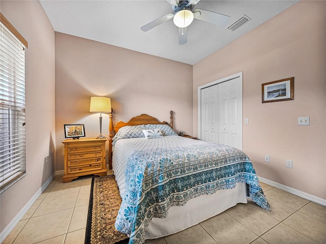 bedroom with baseboards, light tile patterned flooring, visible vents, a ceiling fan, and a closet