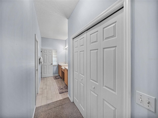 hallway with light carpet, baseboards, and a textured ceiling