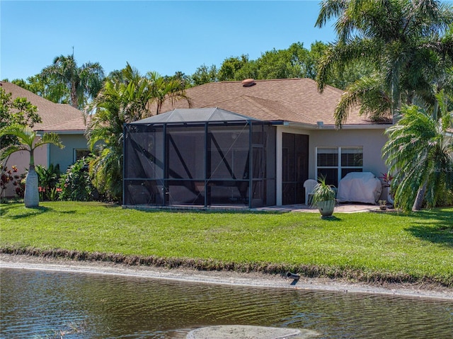 back of house with stucco siding, a water view, a yard, and glass enclosure