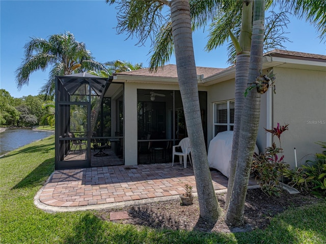 rear view of property featuring a water view, glass enclosure, stucco siding, a yard, and a patio area
