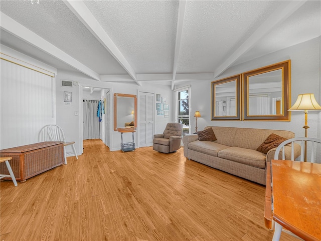 living room with beam ceiling, light wood-style flooring, and a textured ceiling