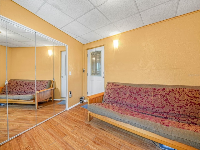 living area featuring a drop ceiling, baseboards, and wood finished floors