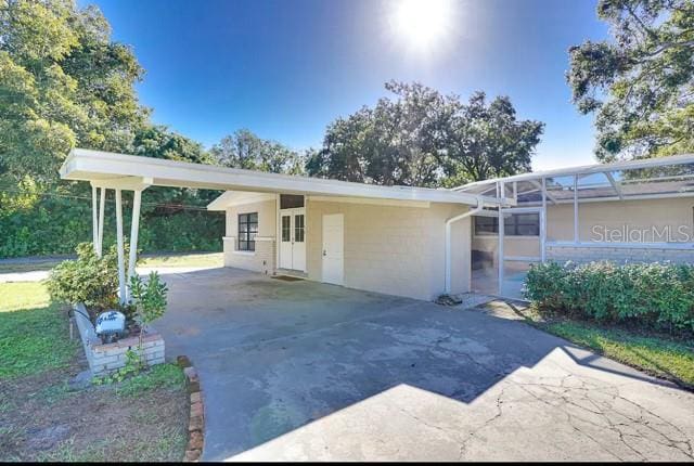 ranch-style home with glass enclosure, an attached carport, and driveway