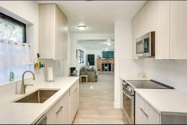 kitchen with tasteful backsplash, a brick fireplace, light countertops, appliances with stainless steel finishes, and a sink