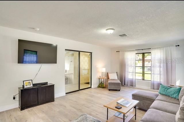 living area featuring visible vents, baseboards, a textured ceiling, and light wood finished floors