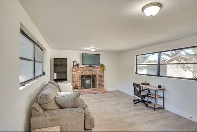 living area with a brick fireplace, light wood-style flooring, and baseboards