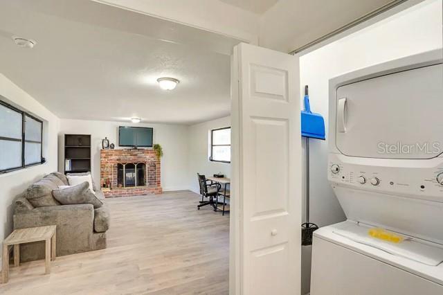 laundry area with laundry area, a brick fireplace, light wood-style floors, and stacked washing maching and dryer