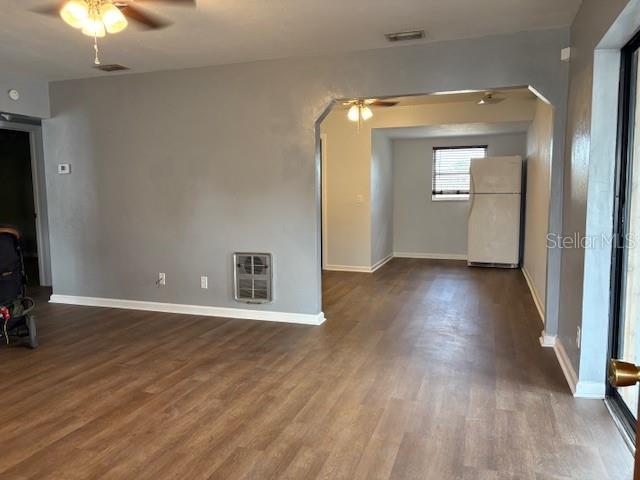 unfurnished living room featuring heating unit, dark wood-style floors, visible vents, arched walkways, and ceiling fan