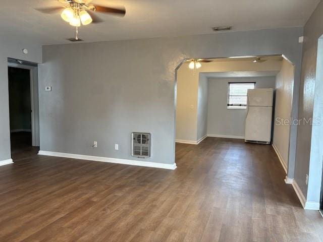 spare room with heating unit, visible vents, arched walkways, dark wood-style flooring, and ceiling fan