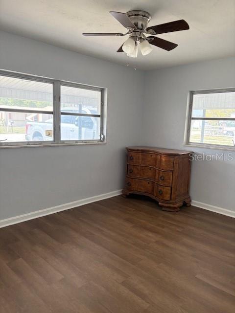 spare room with baseboards, ceiling fan, and dark wood-style flooring