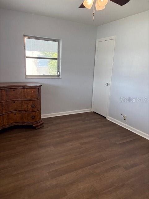 unfurnished bedroom featuring baseboards, a ceiling fan, and dark wood-style flooring