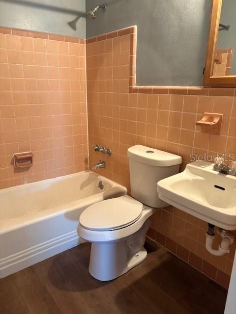 full bath featuring tub / shower combination, toilet, wood finished floors, tile walls, and a sink