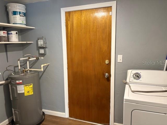 laundry area with dark wood-type flooring, baseboards, water heater, laundry area, and washer / dryer