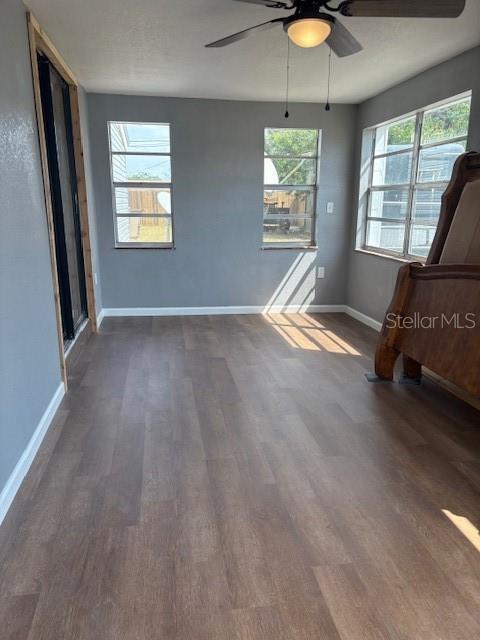 interior space with a ceiling fan, dark wood-style floors, baseboards, and a healthy amount of sunlight