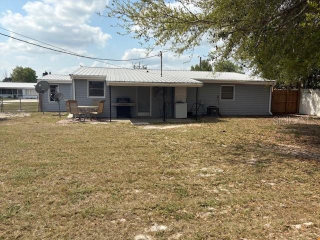 rear view of house with a patio, fence, a lawn, and metal roof