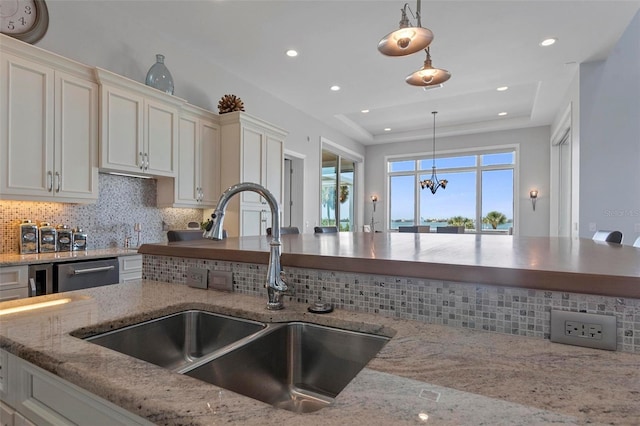 kitchen featuring hanging light fixtures, dishwasher, white cabinetry, and a sink