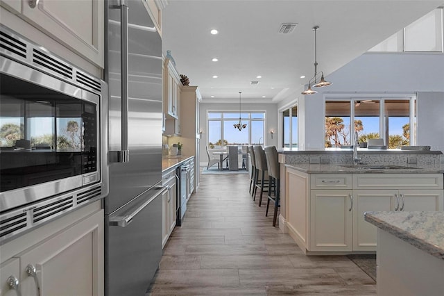 kitchen with visible vents, a sink, a breakfast bar area, built in appliances, and hanging light fixtures