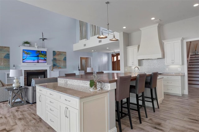 kitchen with a kitchen island with sink, open floor plan, light wood-style floors, a fireplace, and custom exhaust hood