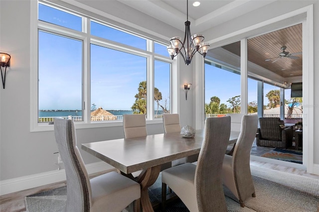 dining room featuring ceiling fan with notable chandelier, wood finished floors, a water view, and baseboards