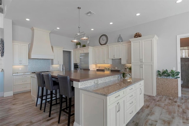 kitchen featuring custom exhaust hood, decorative backsplash, a large island, appliances with stainless steel finishes, and white cabinetry