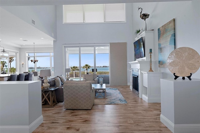 living room with light wood-type flooring, visible vents, a glass covered fireplace, and a towering ceiling