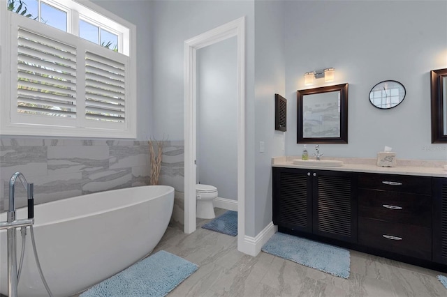 full bathroom with tile walls, a freestanding bath, toilet, marble finish floor, and vanity