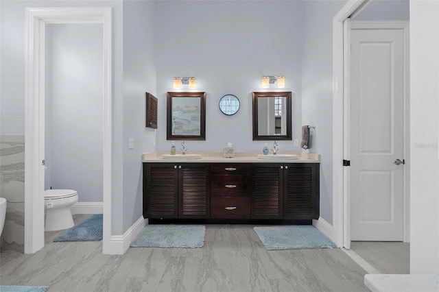 bathroom featuring double vanity, toilet, baseboards, and a sink