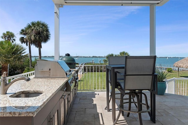 view of patio with an outdoor kitchen, a grill, a water view, and a sink