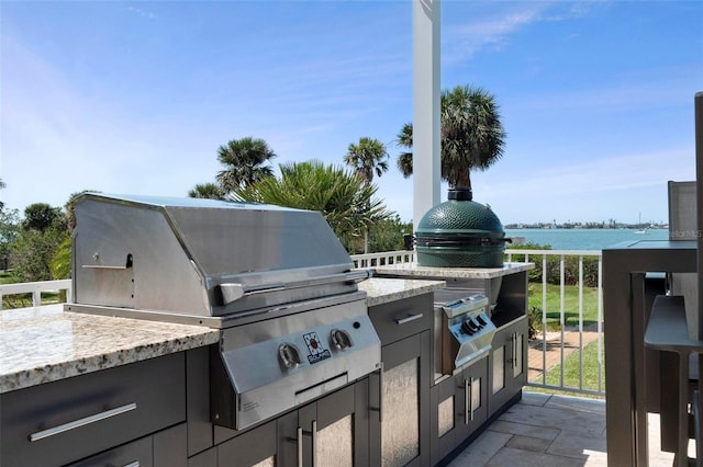 view of patio with grilling area, a water view, and an outdoor kitchen