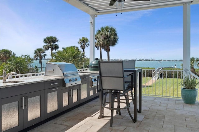 view of patio with a water view, a ceiling fan, a sink, grilling area, and exterior kitchen