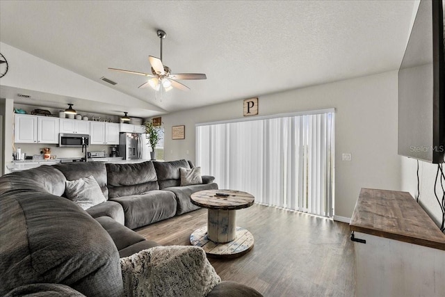 living area with light wood finished floors, visible vents, lofted ceiling, a textured ceiling, and a ceiling fan