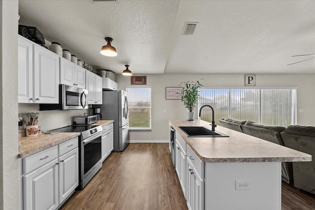 kitchen featuring a sink, dark wood-type flooring, light countertops, stainless steel appliances, and a kitchen island with sink