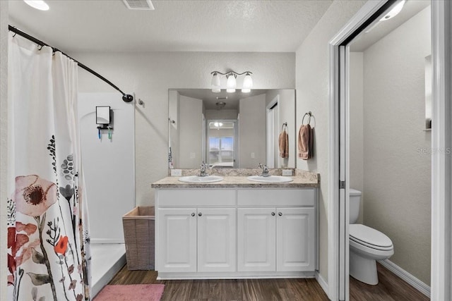 full bathroom with curtained shower, toilet, a textured wall, wood finished floors, and a sink