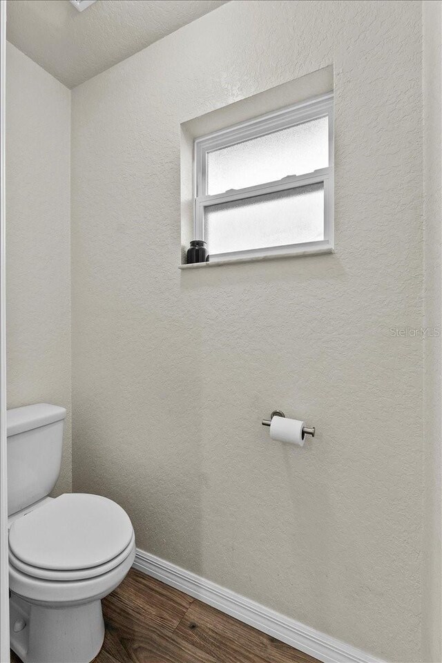 bathroom with a textured wall, toilet, baseboards, and wood finished floors