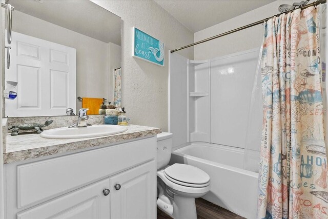 bathroom featuring toilet, a textured wall, shower / tub combo, wood finished floors, and vanity