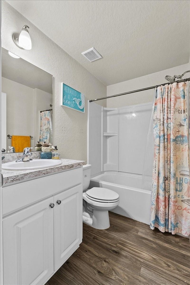 bathroom with visible vents, a textured ceiling, wood finished floors, vanity, and a textured wall