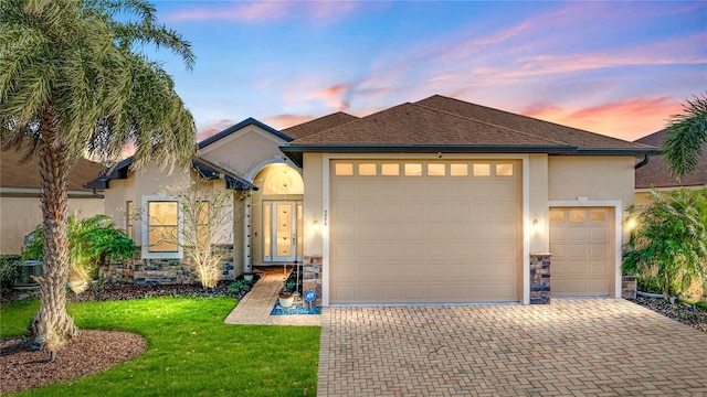 ranch-style house with stucco siding, a front lawn, decorative driveway, a shingled roof, and a garage