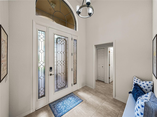 entryway featuring baseboards, a high ceiling, a chandelier, and light tile patterned flooring