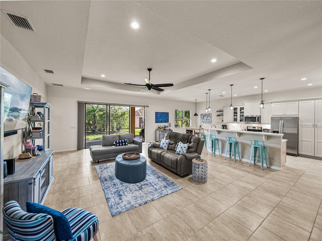 living room with visible vents, recessed lighting, a textured ceiling, and a raised ceiling