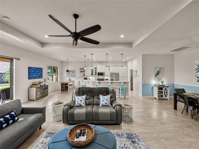 living area featuring baseboards, visible vents, recessed lighting, ceiling fan, and a raised ceiling