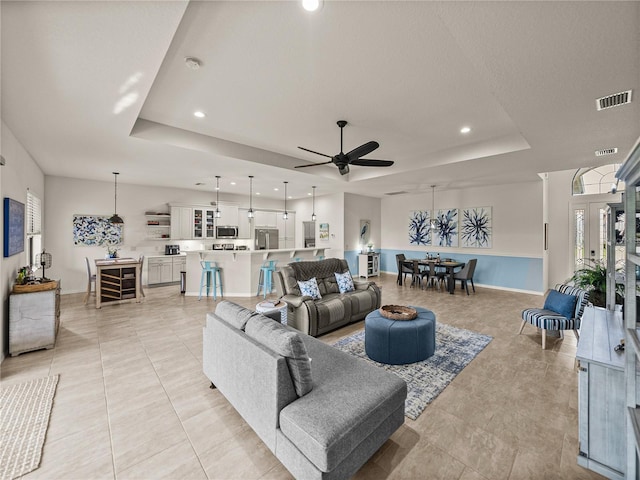 living room with a tray ceiling, recessed lighting, baseboards, and visible vents