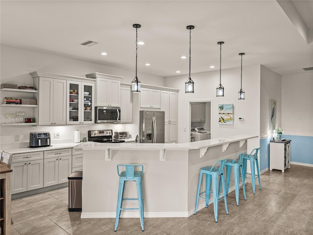 kitchen with washer and dryer, appliances with stainless steel finishes, light countertops, and a kitchen breakfast bar