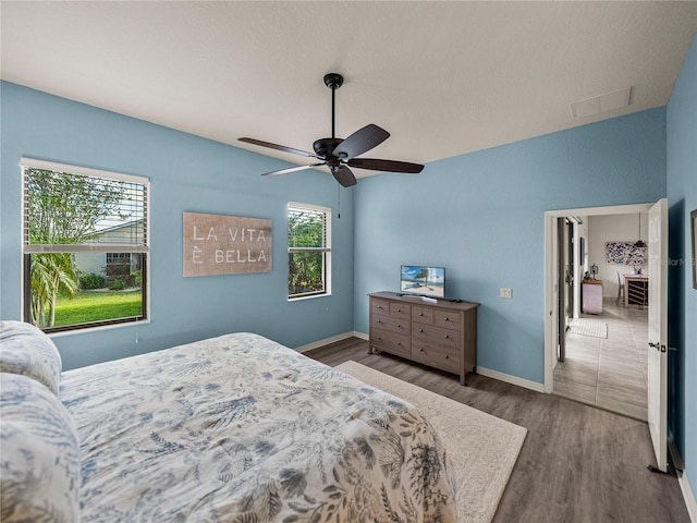 bedroom with a ceiling fan, wood finished floors, visible vents, and baseboards