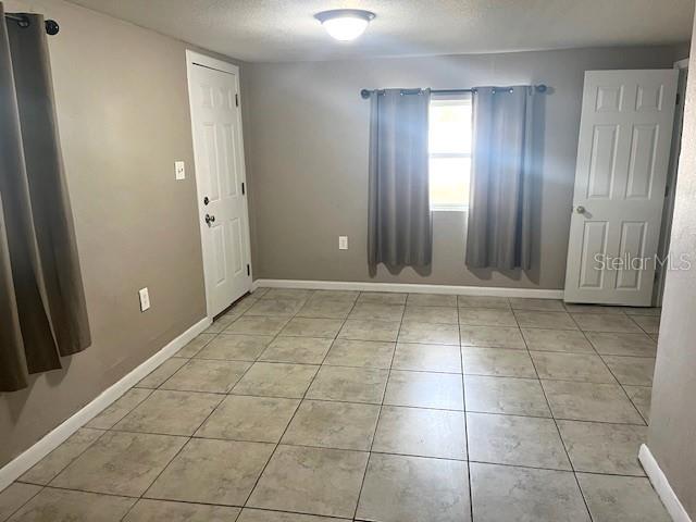 unfurnished room featuring light tile patterned flooring, a textured ceiling, and baseboards