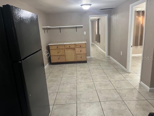 kitchen featuring open shelves, freestanding refrigerator, light countertops, light tile patterned floors, and baseboards