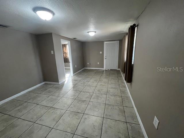 empty room featuring light tile patterned flooring, visible vents, a textured ceiling, and baseboards