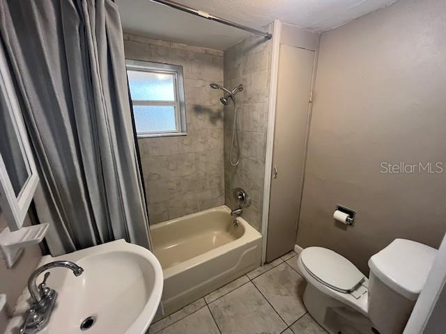 full bathroom with tile patterned flooring, toilet, shower / bath combo with shower curtain, and a sink