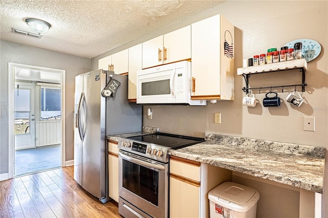 kitchen featuring a textured ceiling, stainless steel electric stove, white cabinetry, light wood finished floors, and white microwave