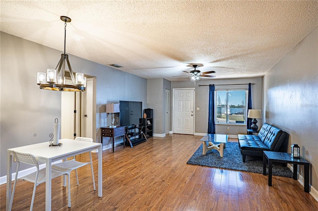 living area with visible vents, ceiling fan with notable chandelier, a textured ceiling, wood finished floors, and baseboards